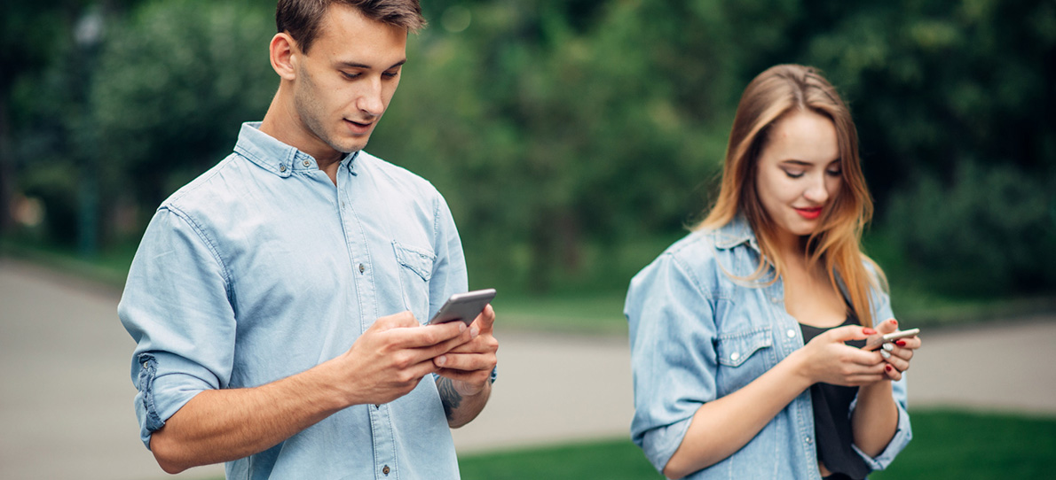 Mann und Frau stehen nebeneinander und schauen auf ihre Handys – symbolisiert den vorsichtigen ersten Kontakt nach einer Kontaktsperre.