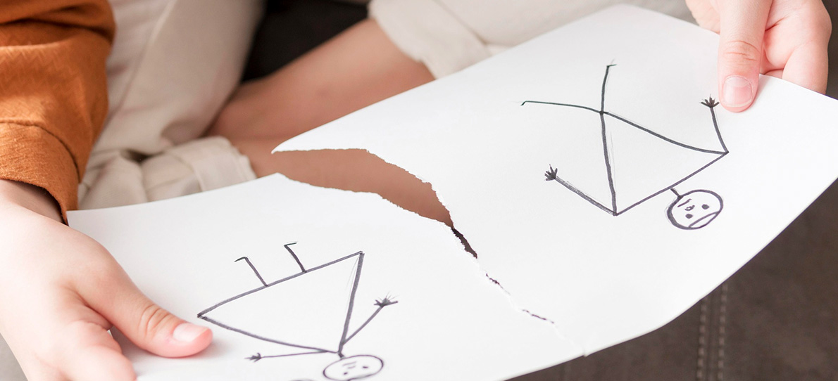 Hände halten ein zerrissenes Blatt mit einer Strichzeichnung eines Paares – symbolisiert den emotionalen Prozess des Loslassens nach einer Trennung.